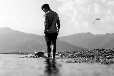 ION Water wetshirt manga comprida homem durante kitesurf em praia com montanhas ao fundo