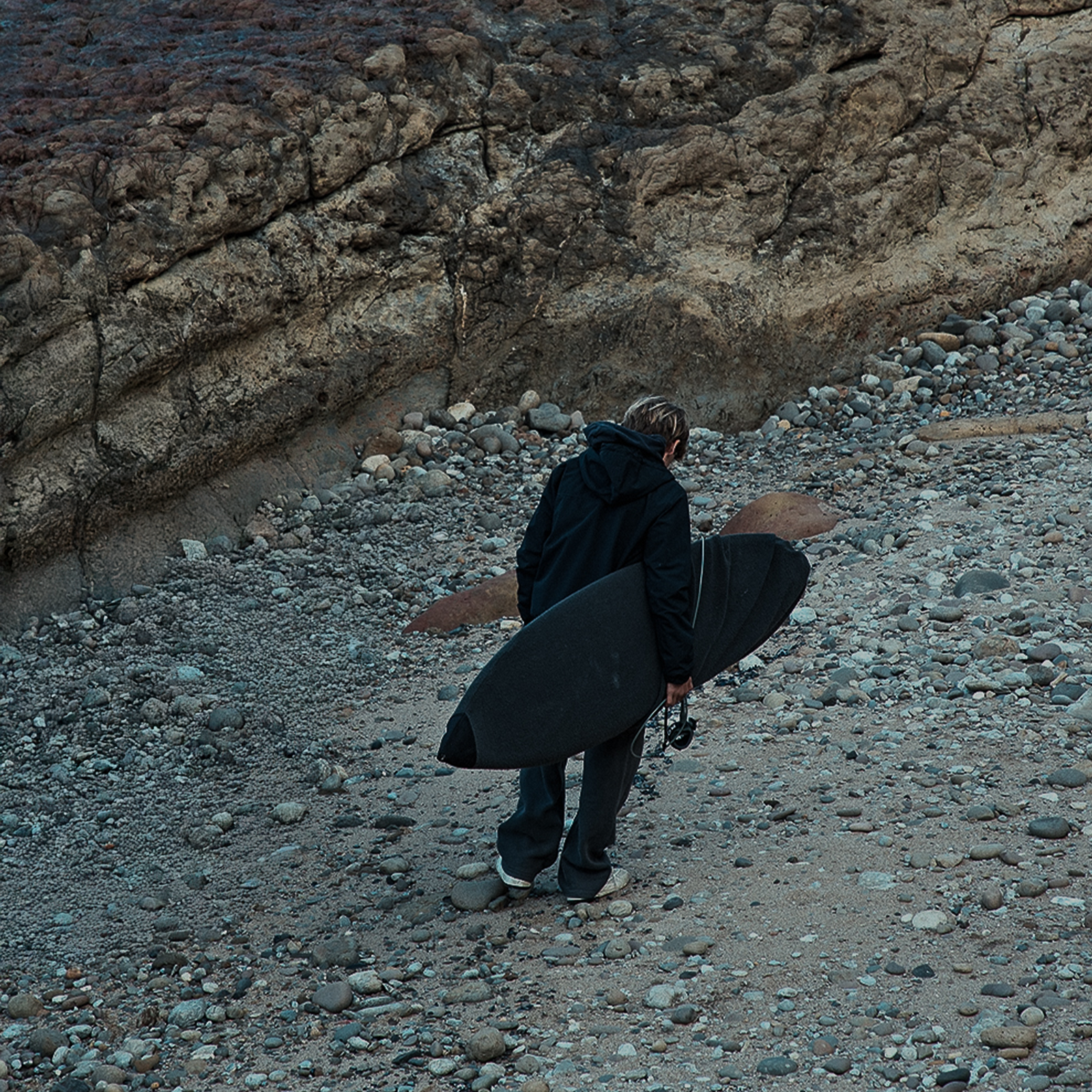 ION Surf Sock board cover 5'9" in black carried at a rocky coastal beach