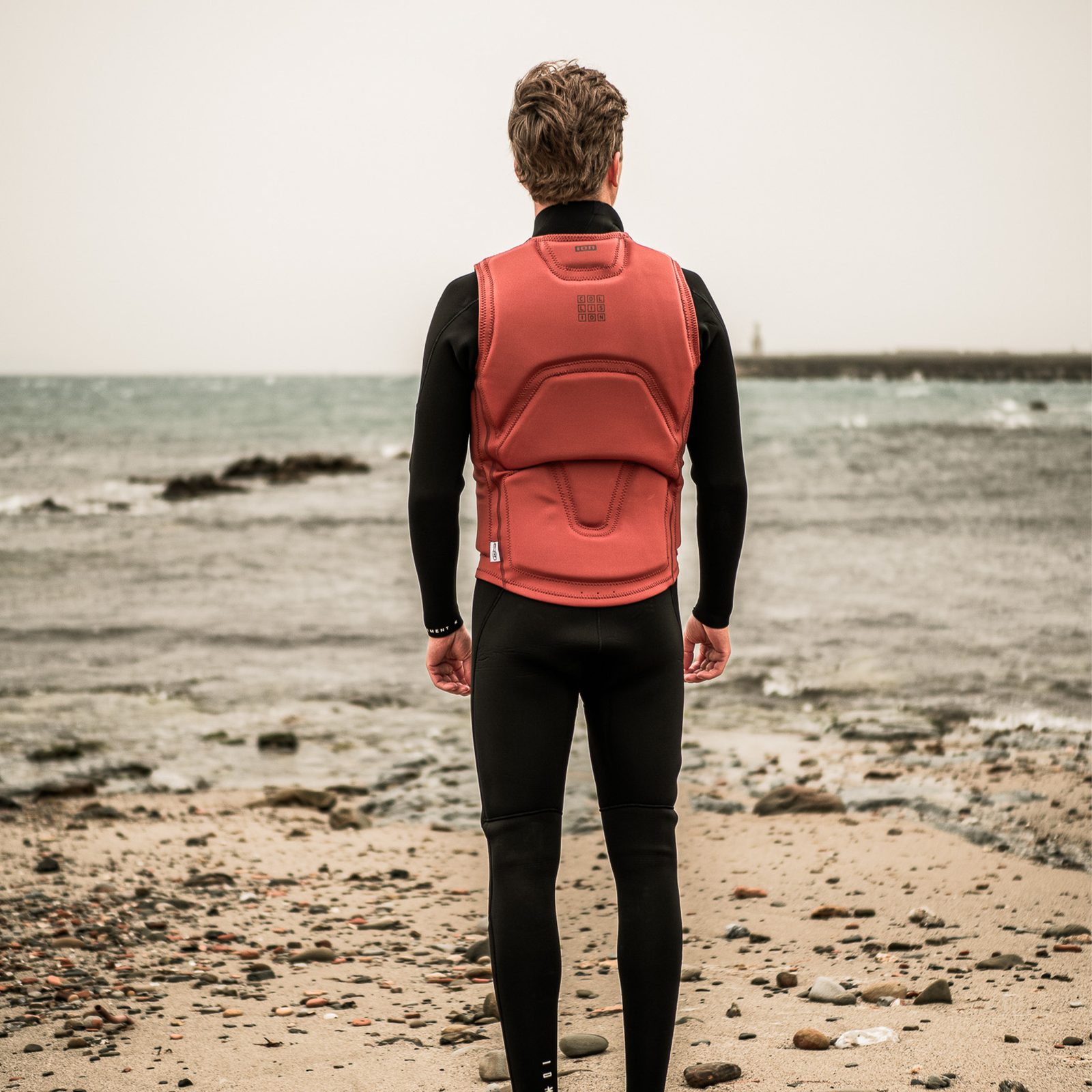 ION Collision Vest Core gilet d'impatto zip frontale uomo in terracotta, vista posteriore sulla spiaggia