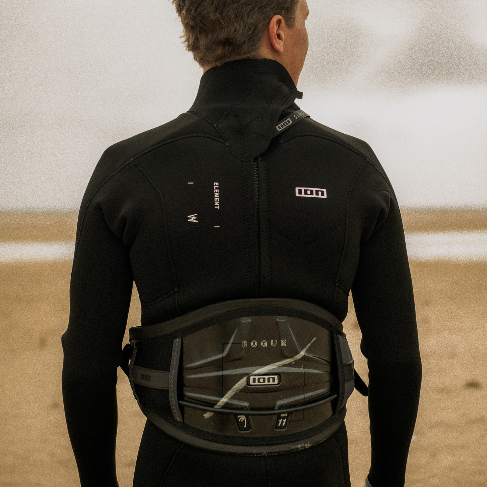 ION Rogue waist harness in black during wing foiling at the beach – back view