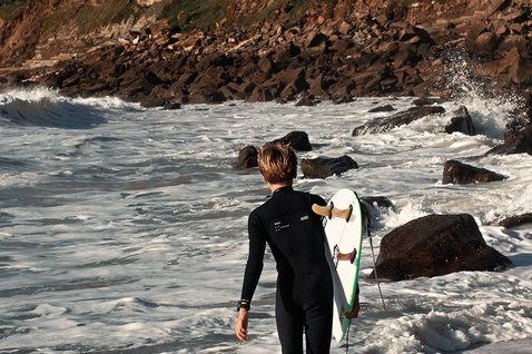 ION Capture Amp 4/3mm front-zip junior fullsuit in black during wave surfing at a rocky beach