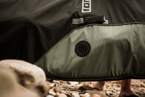 ION Wing Boardbag Core Slim boardbag in black and olive green at a rocky beach during wing foiling
