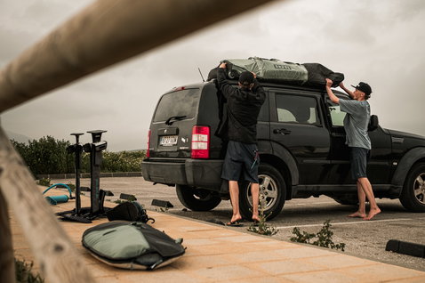 ION Gearbag Core kite gear bag being loaded onto a 4x4 roof rack at the coast