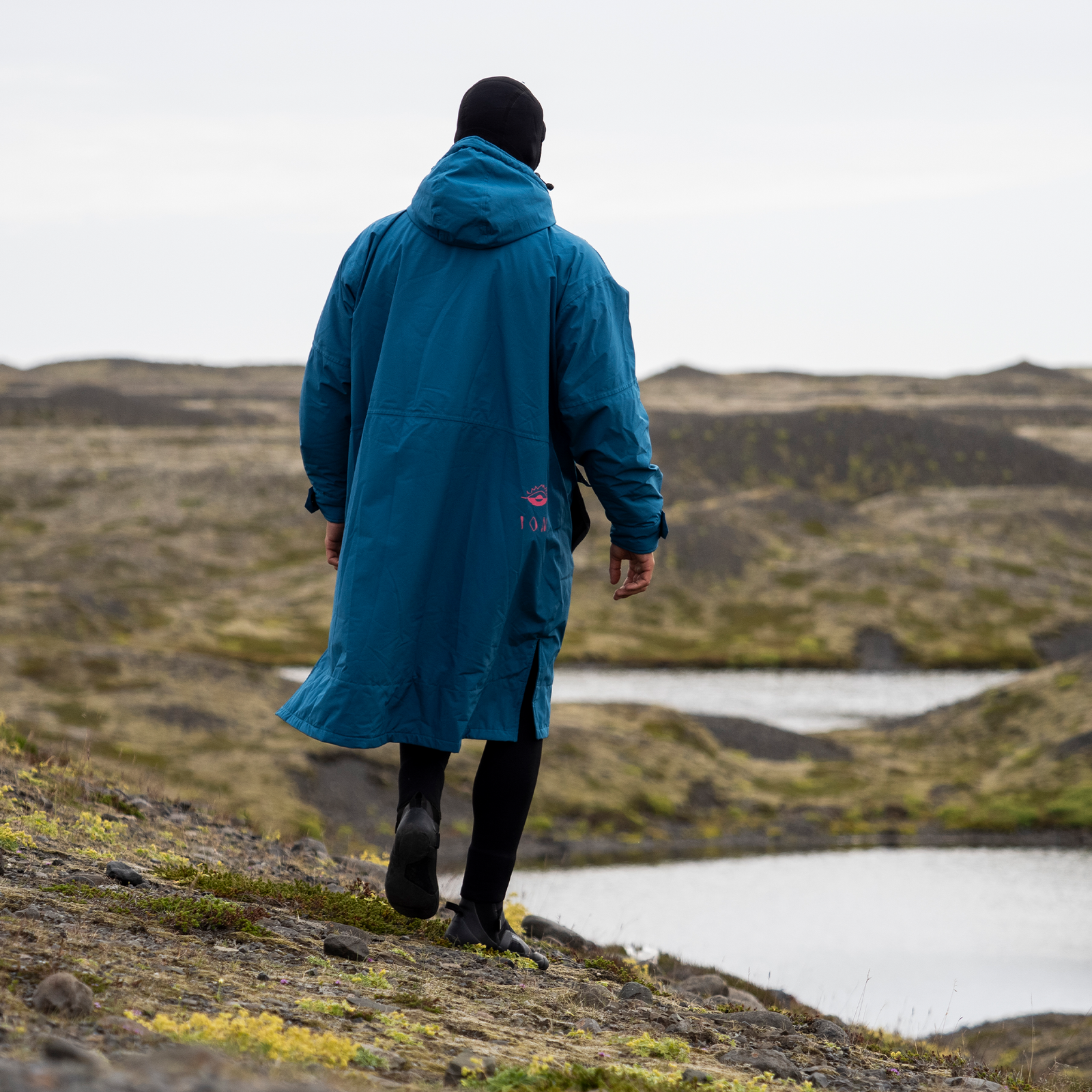 ION Water Storm Coat jacket in teal blue during a walk along a rocky coastal landscape