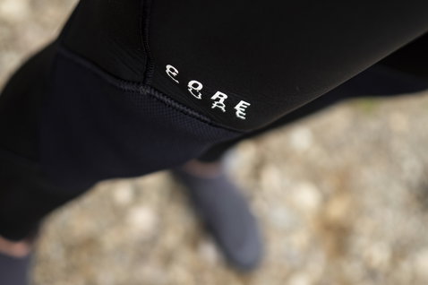 ION Seek Core 5/4 mm Back-Zip Neoprenanzug in schwarz – Hip-Detail mit CORE-Logo an felsiger Küste