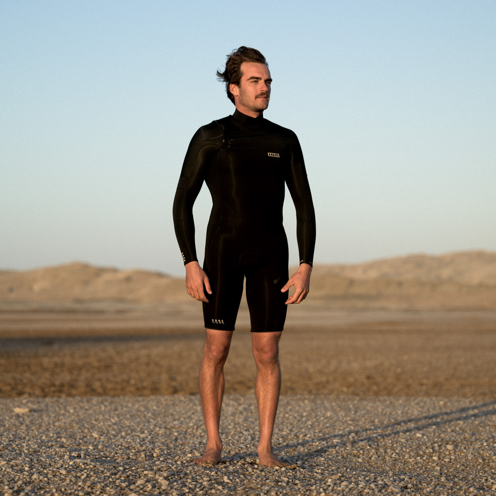 ION Seek Core 3/2mm front-zip long sleeve shorty wetsuit men in black on sandy beach