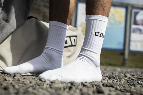 Chaussettes longues unisexes ION Ionic en blanc avec logo noir, portées en extérieur sur graviers
