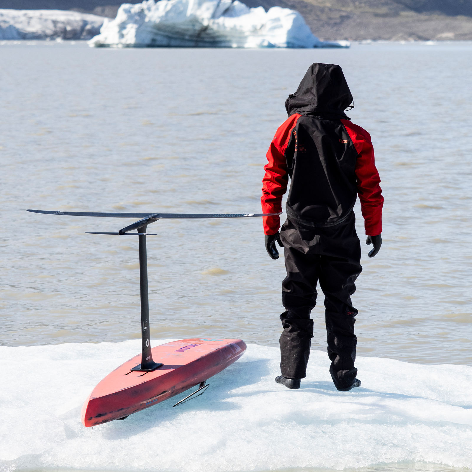 ION Fuse Lightweight back-zip drysuit in black and red during wing foiling on an arctic glacier lake