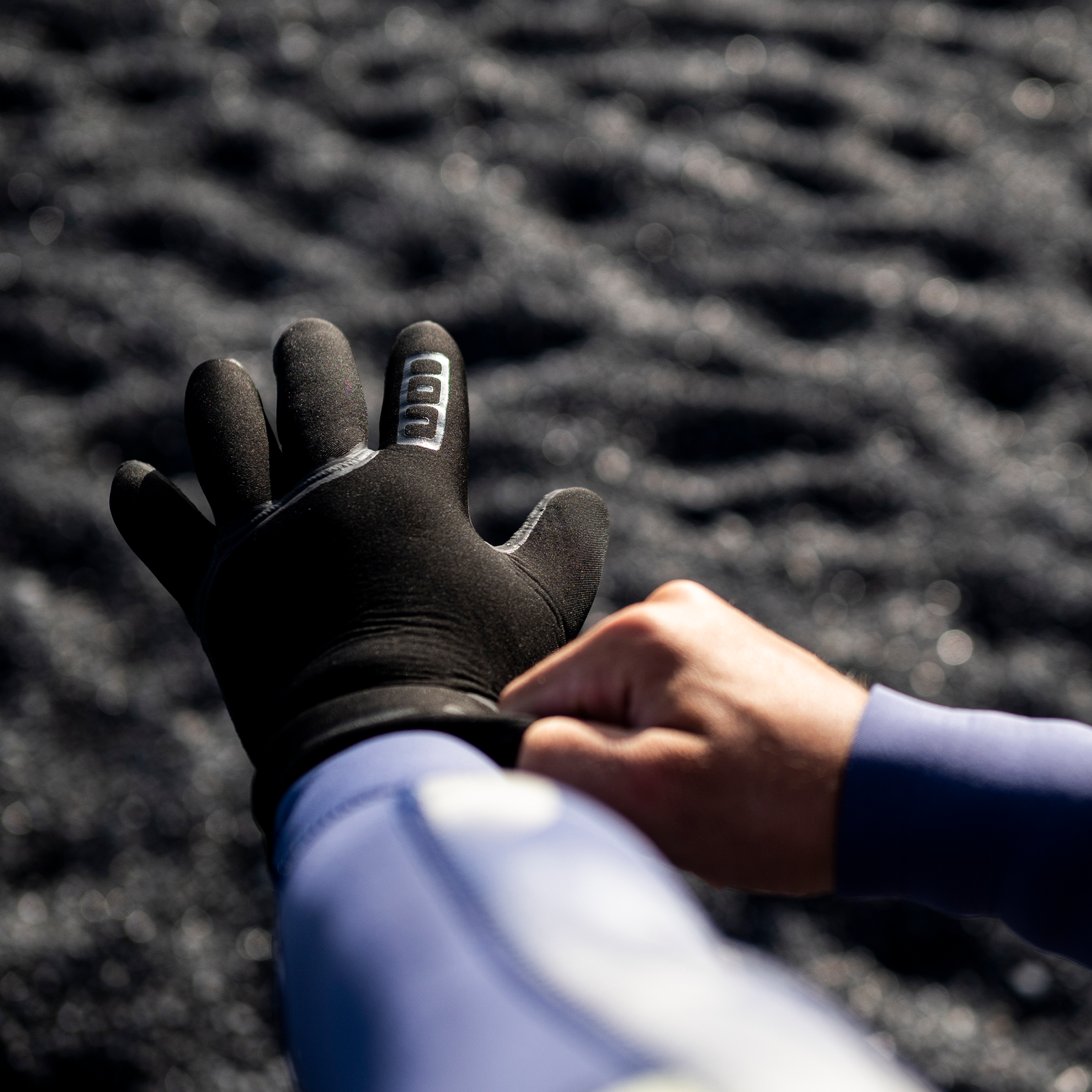 Gants en néoprène ION Neo 4/2mm en noir en cours d'enfilage sur la côte