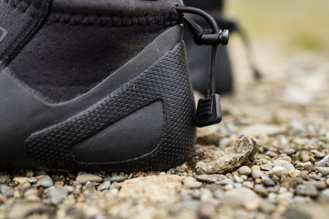 ION Plasma Shoes 2.5 Round Toe neoprene boots in black during kitesurfing on a rocky beach