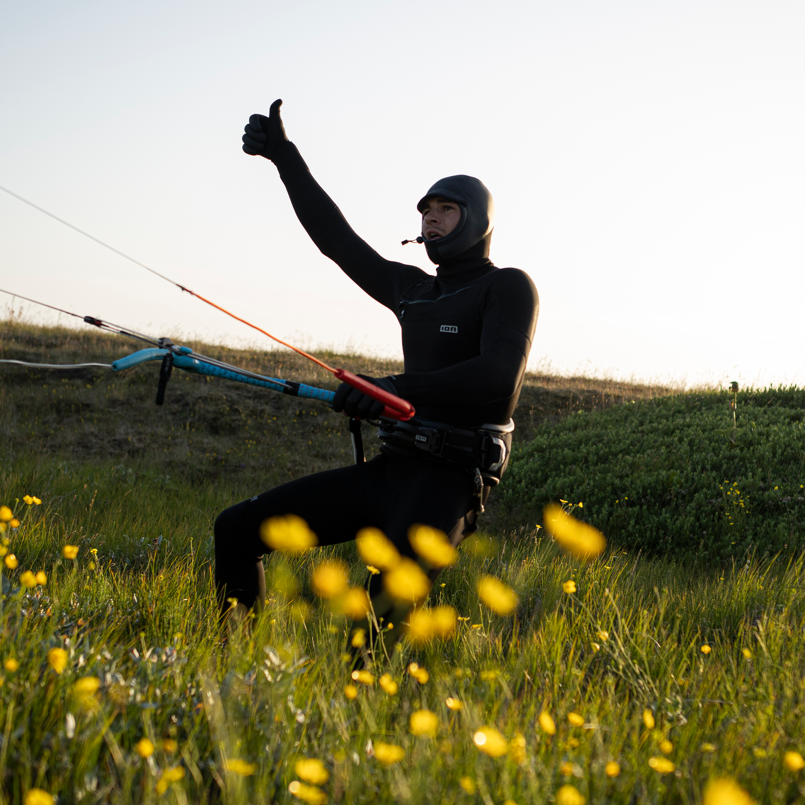 Arnês de cintura ION Spectre com casco rígido em carbono durante kitesurf em prado florido ao pôr do sol