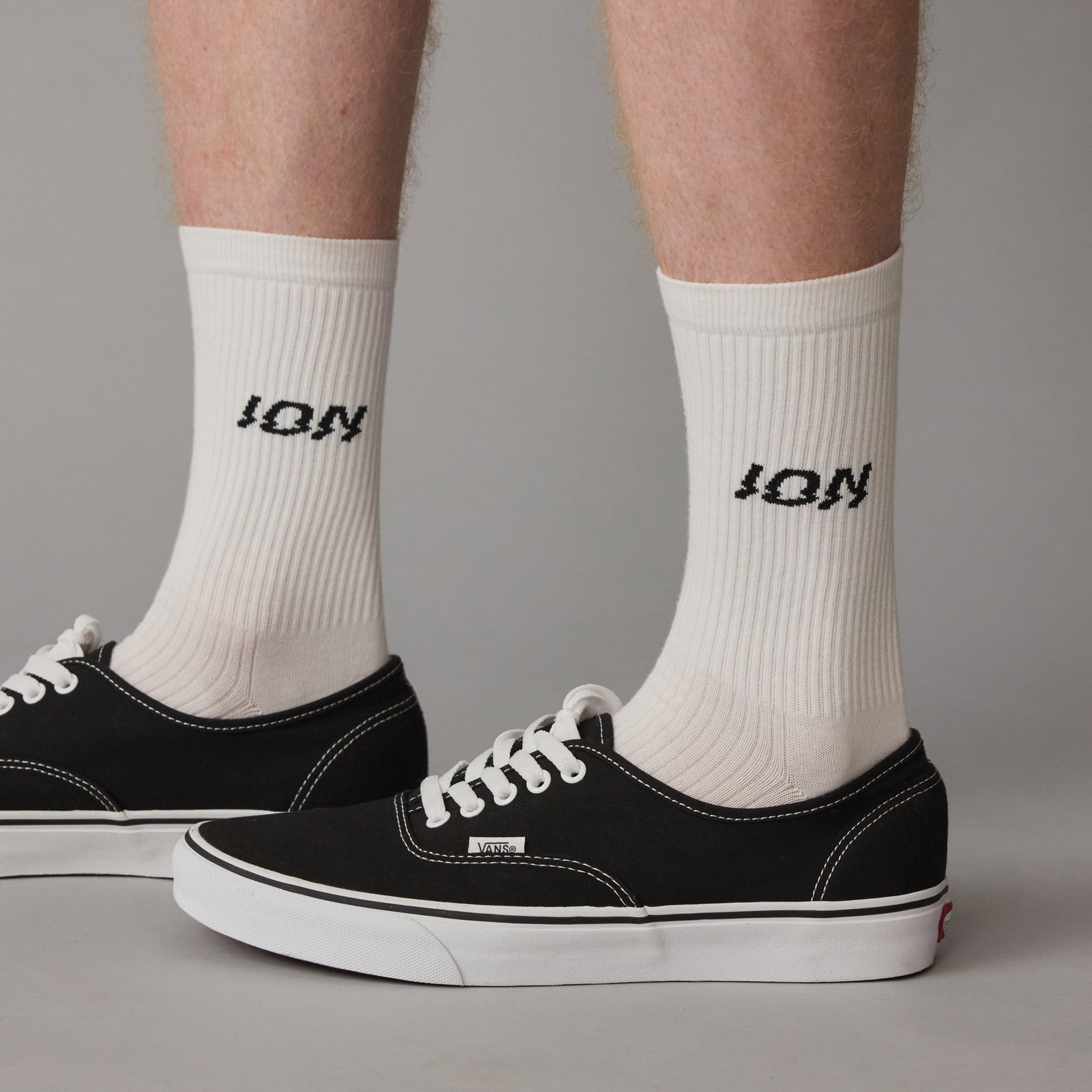 ION Ionic Light unisex crew socks in white with black logo, worn with black sneakers