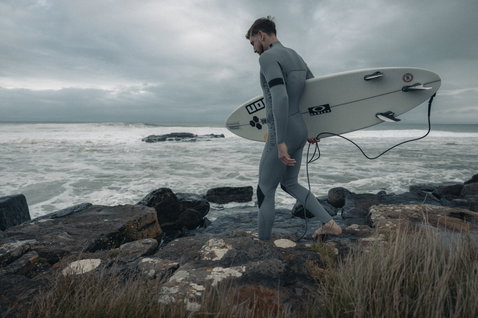 Muta ION Seek Core 4/3mm con zip frontale in grigio antracite durante il surf su costa rocciosa