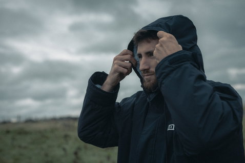 ION Water Jacket Storm Coat Unisex in dunkelblau beim Tragen an der Küste bei stürmischem Wetter