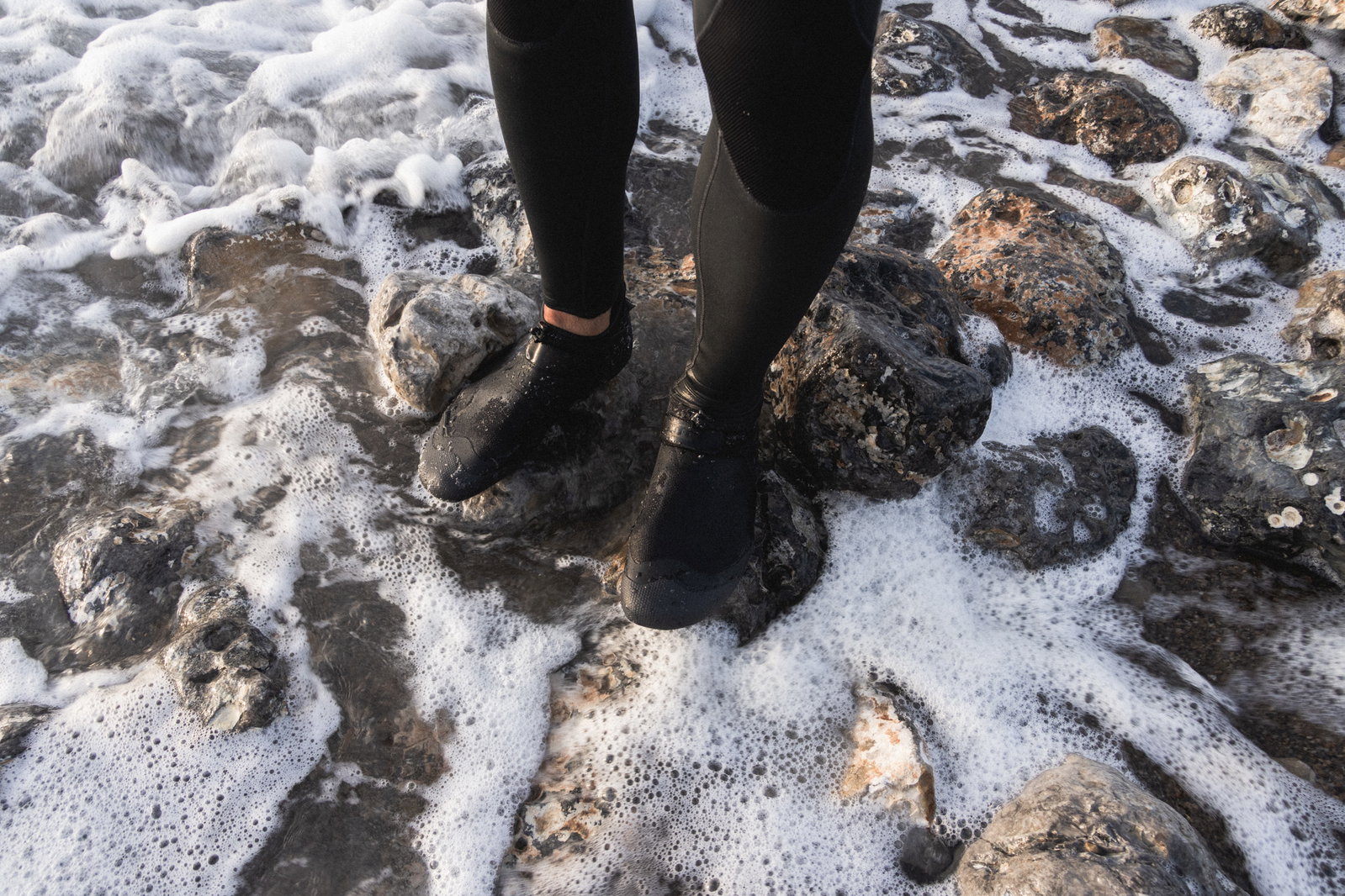ION Ballistic Shoes 2.5 neoprene boots in black during kitesurfing on a rocky shoreline