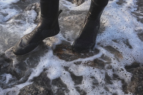 ION Plasma Boots 6/5 Round Toe neoprene boots in black during kitesurfing at a rocky shoreline