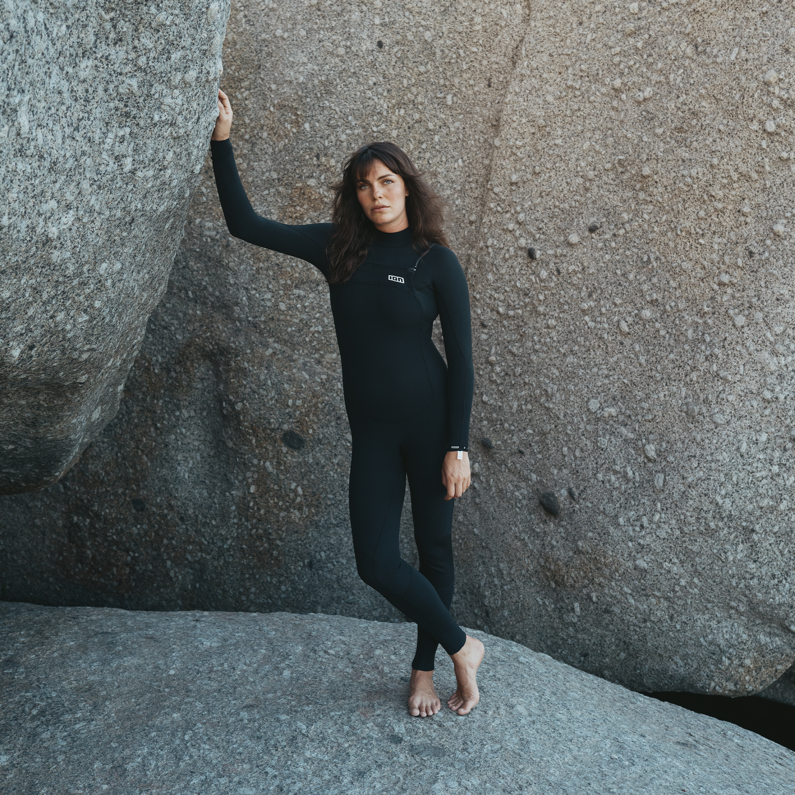 ION Static muta integrale 3/2 mm zip frontale donna in nero indossata su rocce costiere