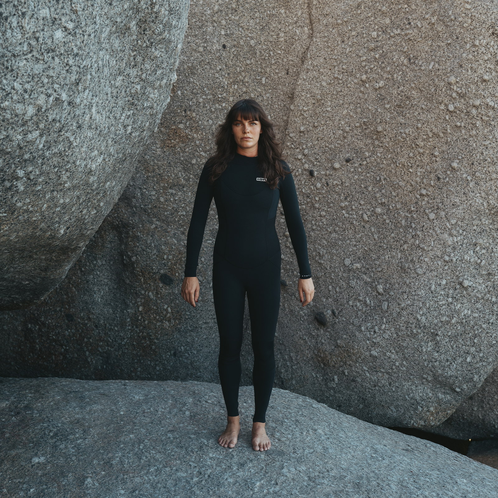 ION Static muta donna 3/2mm zip posteriore in nero indossata su costa rocciosa