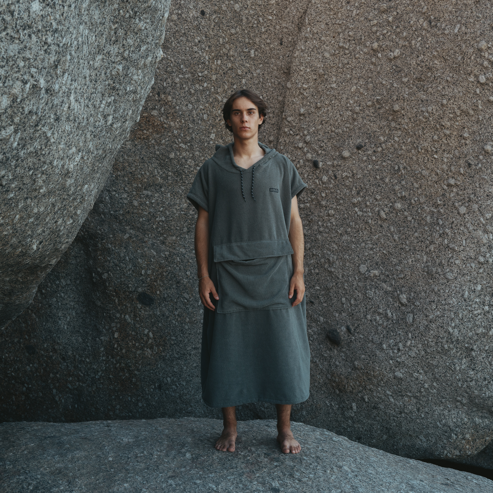 ION Element surf poncho in dark slate grey worn on rocky coastal boulders