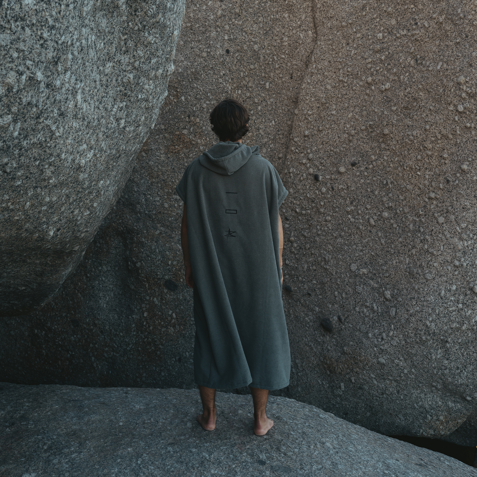 ION Element surf poncho in dark slate grey worn on rocky terrain – back view