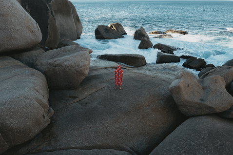 ION Core Lumen surf poncho in red all-over print worn at a rocky coastline
