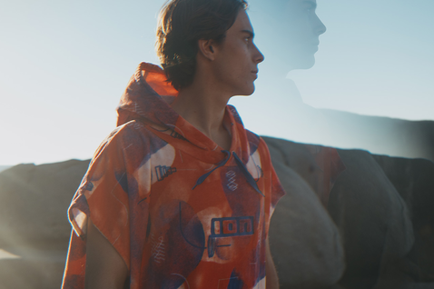 ION Poncho Core surf poncho in orange with graphic print worn at the coast