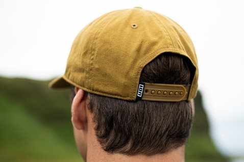 ION Session snapback cap in mustard yellow worn from behind at the coast