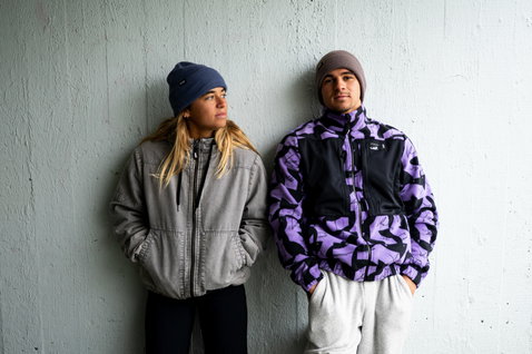 ION Ionic beanie taglia unica in blu navy e taupe indossato da due persone davanti a un muro grigio