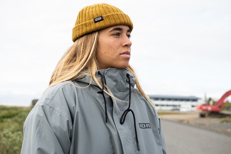 ION Ionic Fisherman beanie in gold burst indossato da una donna sulla costa