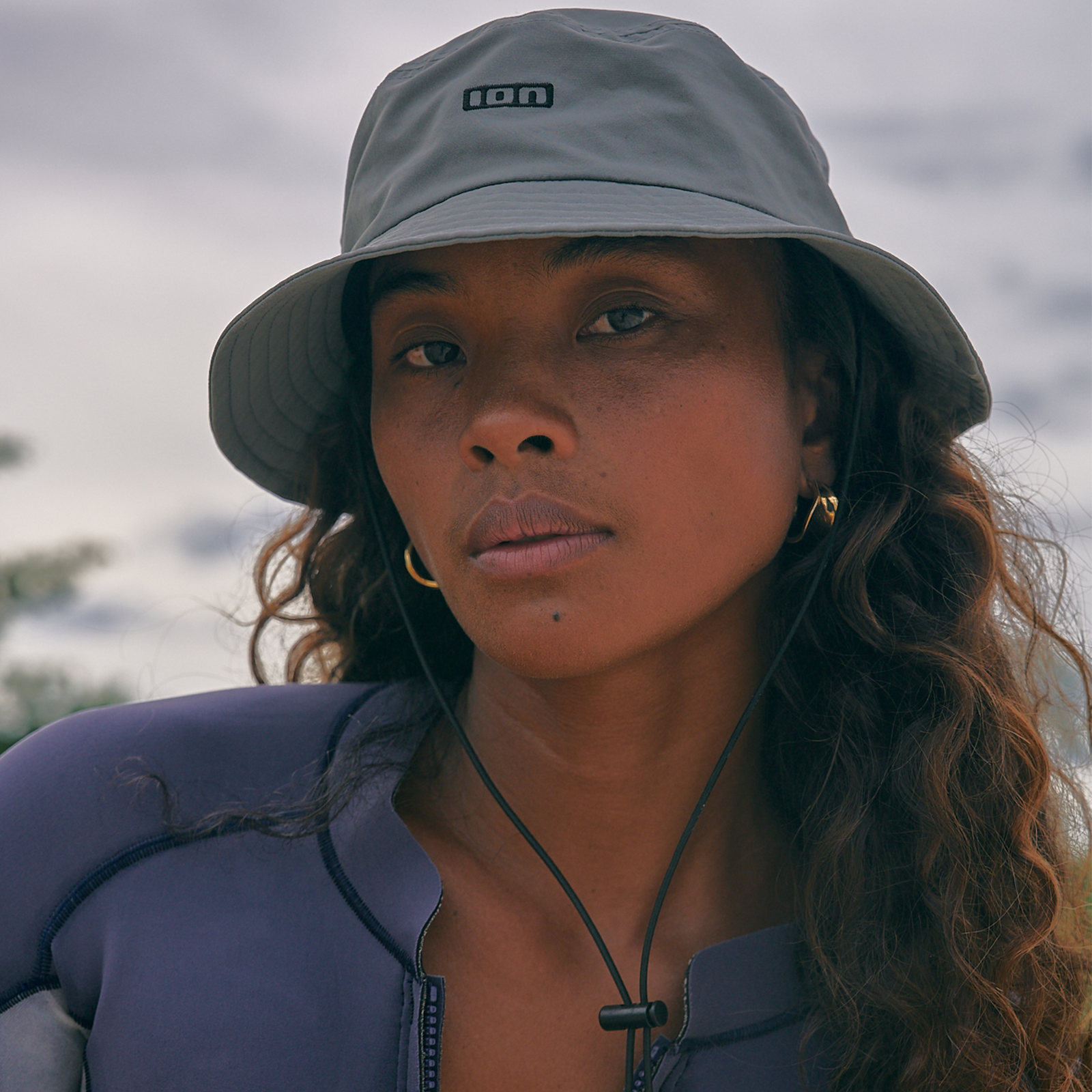 ION Water Cap Bucket Surf Hat in grigio indossato da una donna in riva al mare con laccetto