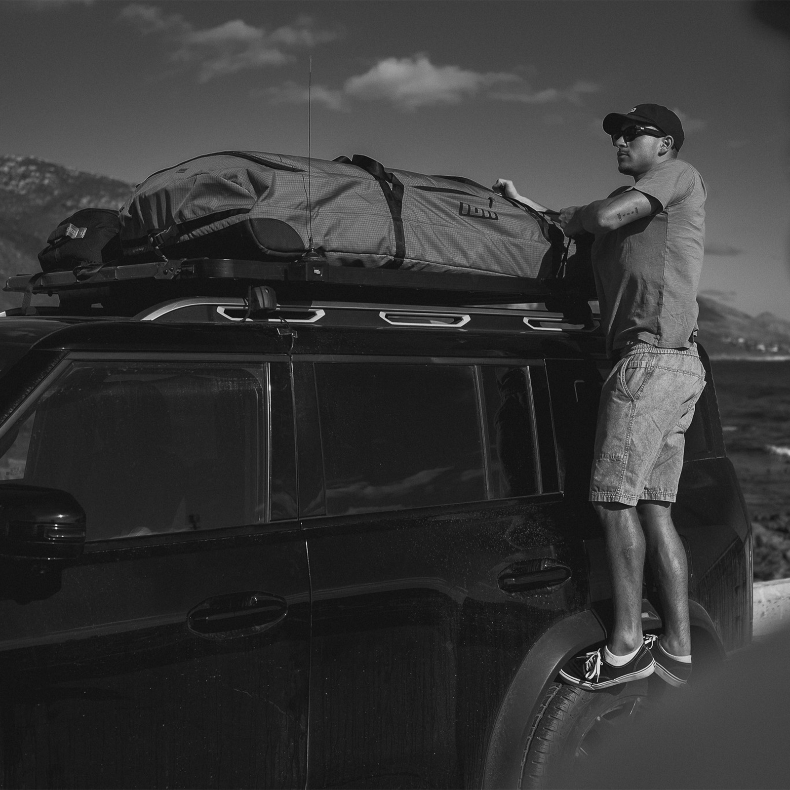 ION Wing Gearbag Core travel bag being loaded onto a vehicle roof rack in a mountain landscape