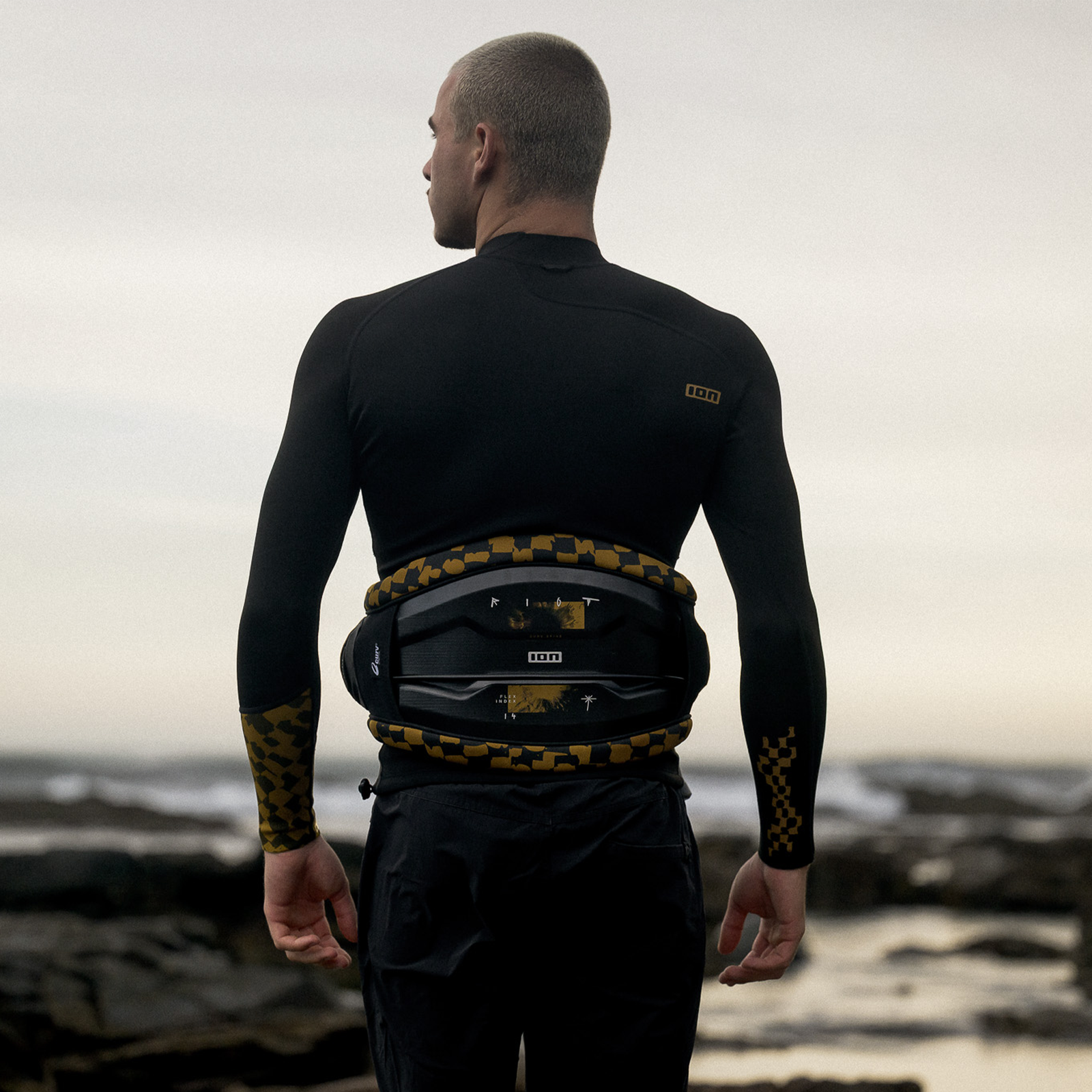 ION Riot Curv waist harness in black and gold during kitesurfing at a rocky coastline