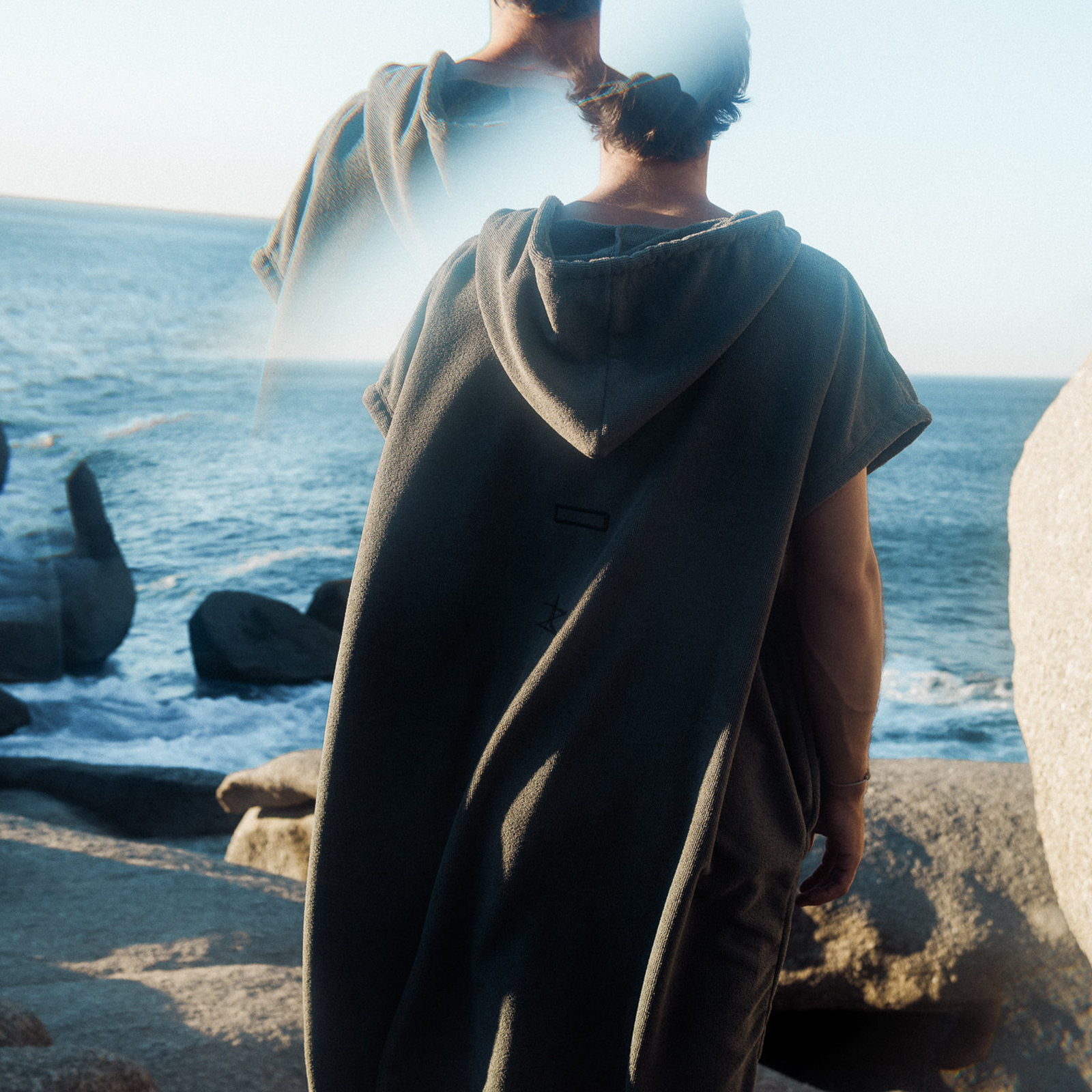 ION Element quick-dry poncho in charcoal grey worn at a rocky coastline