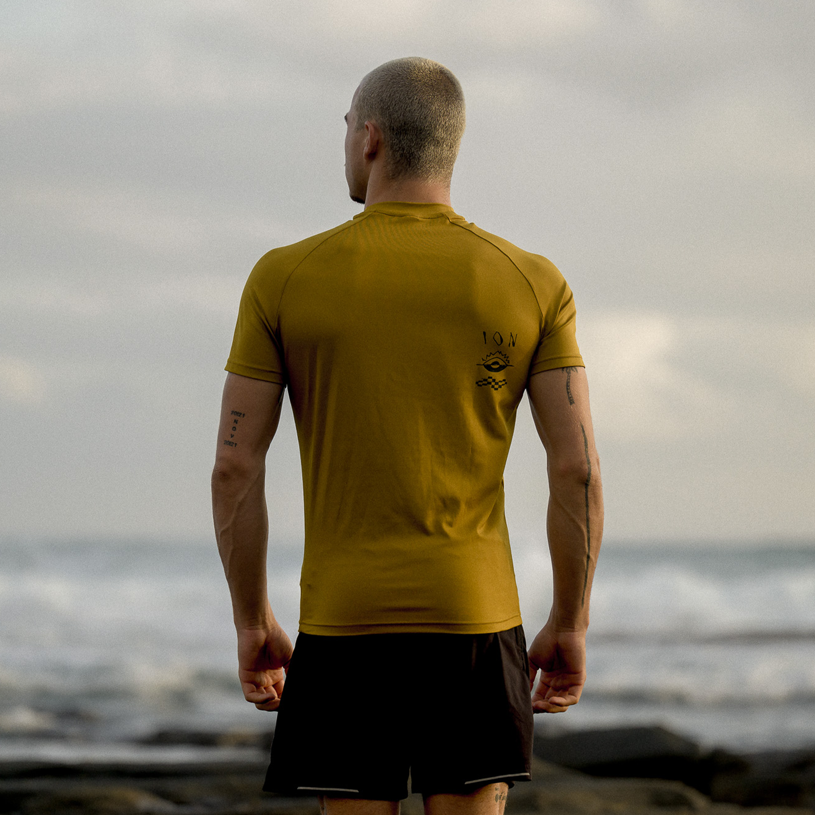 ION Rashguard SS homme manches courtes en olive doré porté de dos sur côte rocheuse