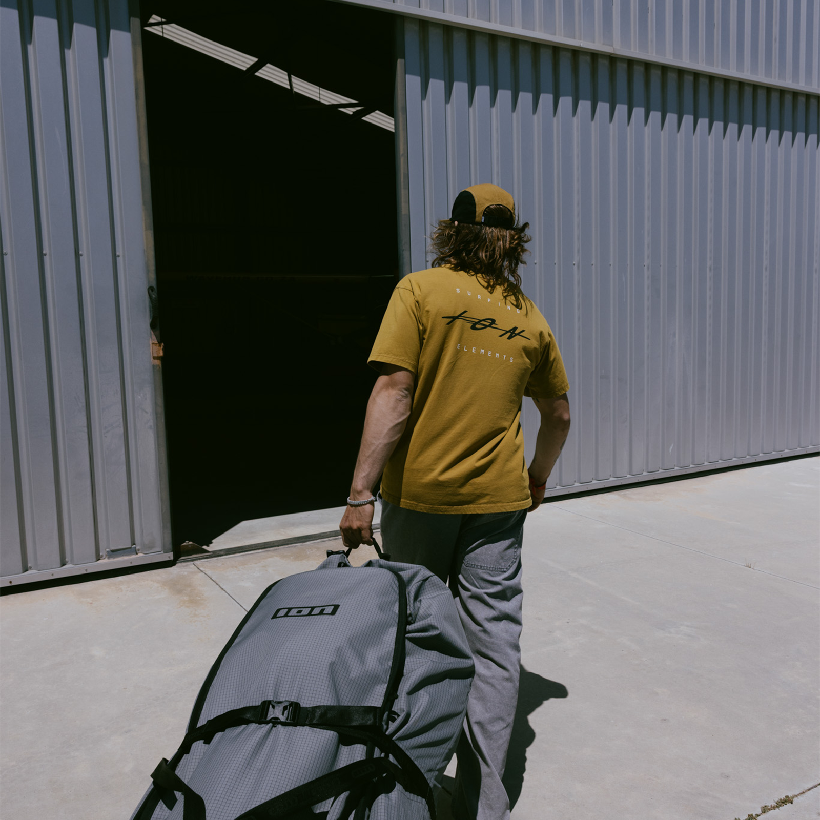 ION Mood SS men's t-shirt in goldburst worn by model carrying an ION board bag