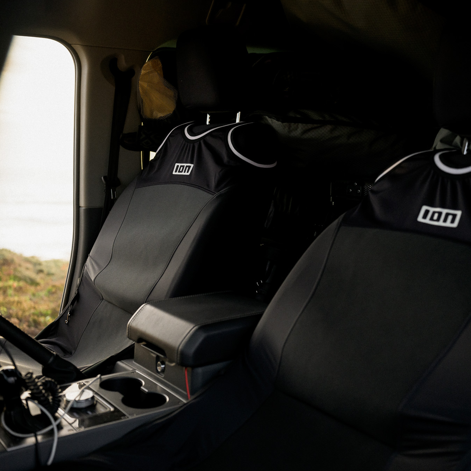 ION Tank Top Seat Cover in black fitted on car front seats, interior lifestyle shot near coastal setting