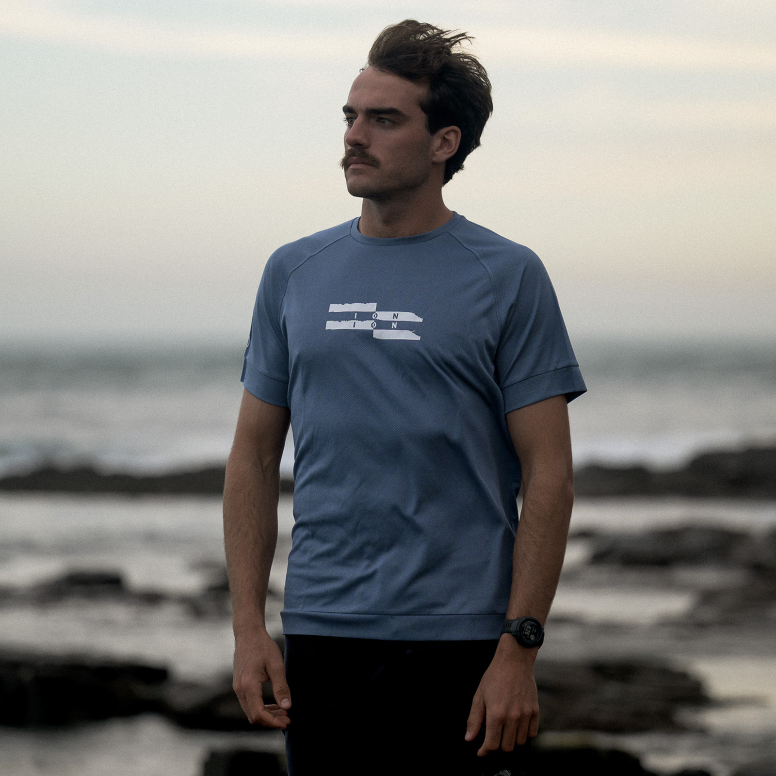 ION Wetshirt SS men short-sleeve rash guard in slate blue worn at a rocky ocean beach