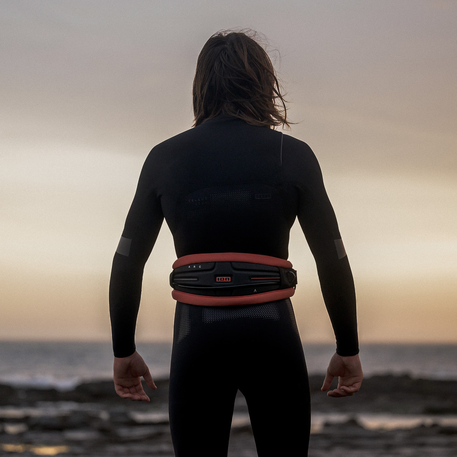 ION Arc waist harness in black and coral during wing foiling at the coast