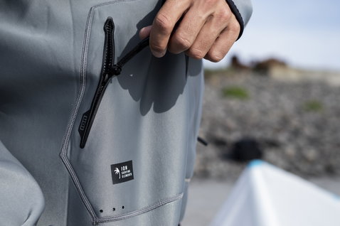 ION Neo Hoody Lite top néoprène homme en gris acier – détail de la poche lors du kitesurf sur la côte