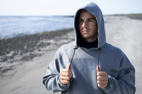 ION Neo Hoody Lite hoodie néoprène en gris acier porté par un homme sur une plage en Islande