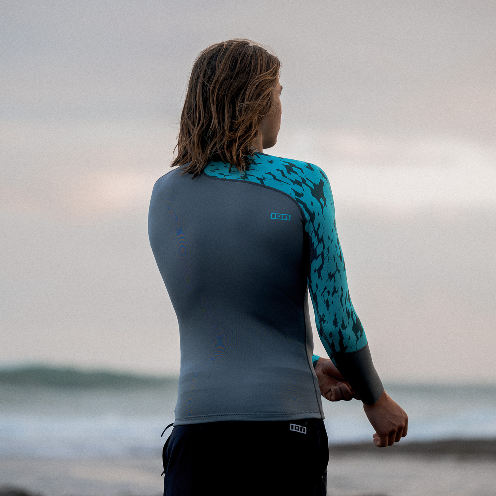 ION Neo Top 0.5 LS men's neoprene long sleeve top in dark grey and teal during kitesurfing at the ocean