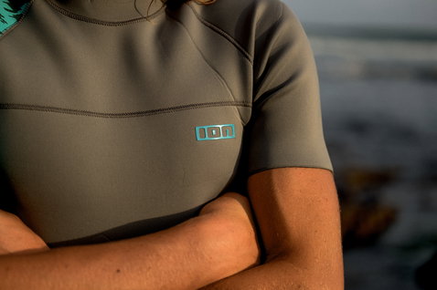 ION Neo Top 2/2 top de neoprene de manga curta masculino em cinzento olive com logótipo turquesa durante desporto aquático na costa