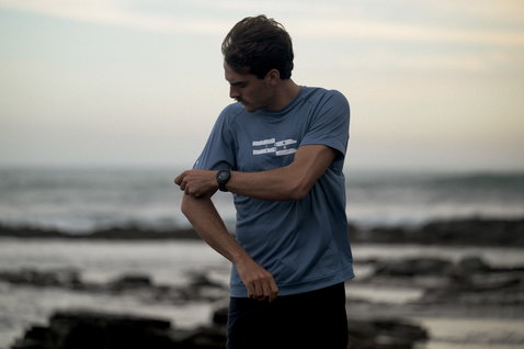 ION Wetshirt short sleeve men in slate blue worn on a rocky beach at dusk