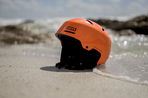 Casco ION Slash Amp in arancione sulla sabbia bagnata in riva al mare