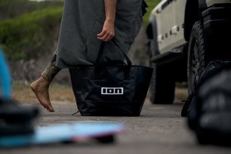 ION Changing Bucket bag in black carried at a coastal watersports location