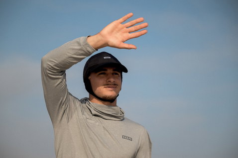 ION Water Cap casquette de surf en noir portée par un homme en extérieur sous un ciel bleu