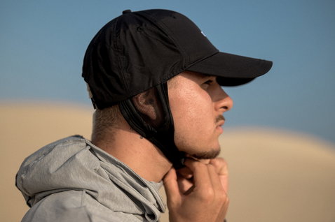 ION Water Cap casquette surf en noir portée en extérieur avec réglage jugulaire sur dunes