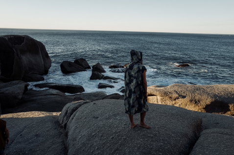 ION Element poncho during beach session on rocky coast in dark charcoal with abstract print