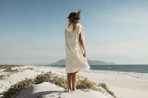 ION Reefside Select poncho in off-white worn at the beach on white sand dunes with ocean view