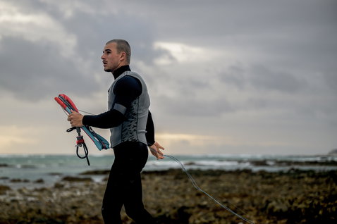 ION Vector Vest Core front-zip men's impact vest during kitesurfing at a rocky ocean coast in dark navy and grey